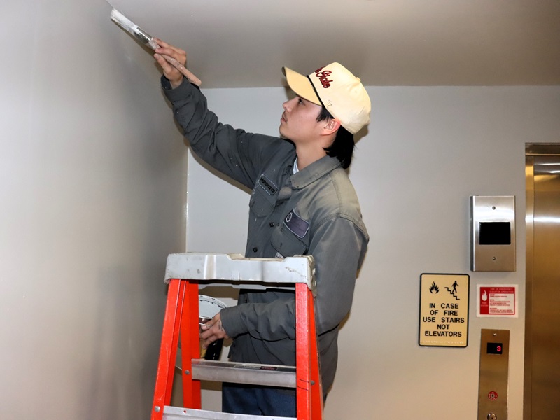 Building Trades Technician Dillan Ly painting a fresh coat in an elevator vestibule